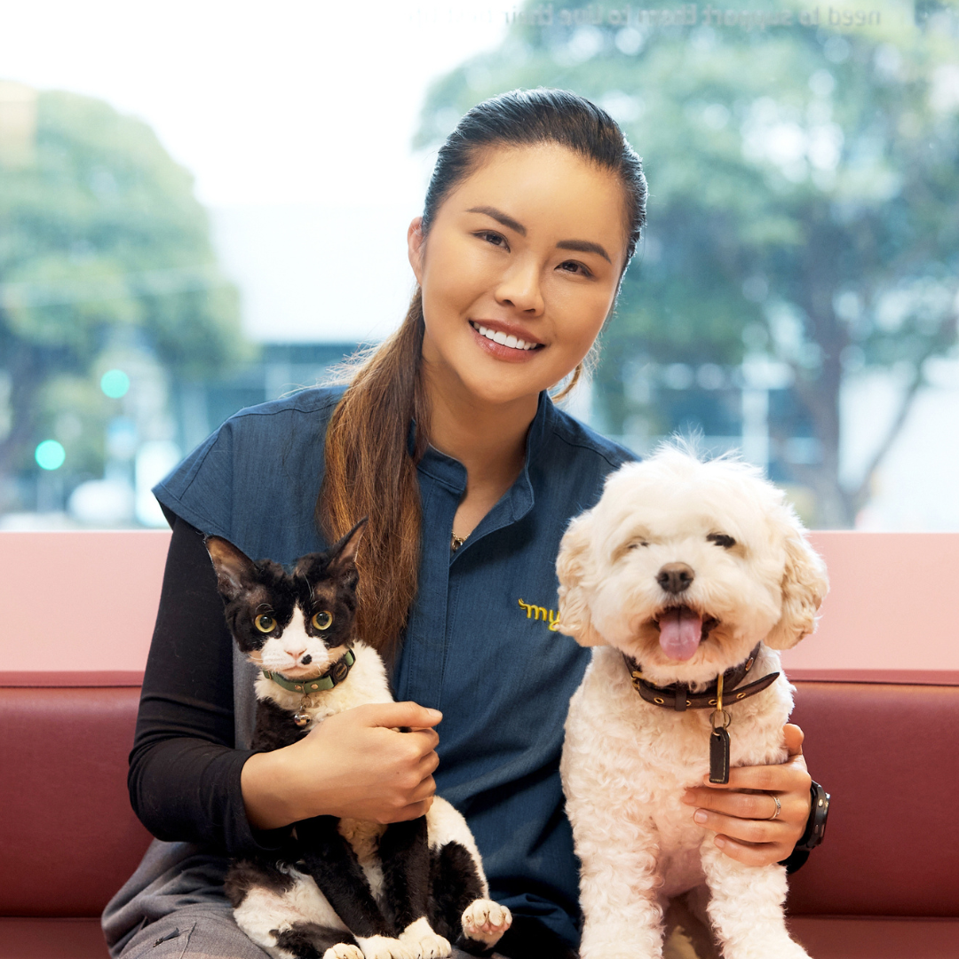 Veterinarian Dr. Cherlene Lee sitting on a bench with a black and white cat and a white dog.